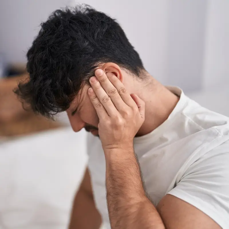 Young hispanic man suffering for backache sitting on bed at bedroom